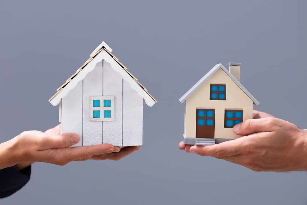 Hands of two people holding model homes in their hands preparing to exchange properties